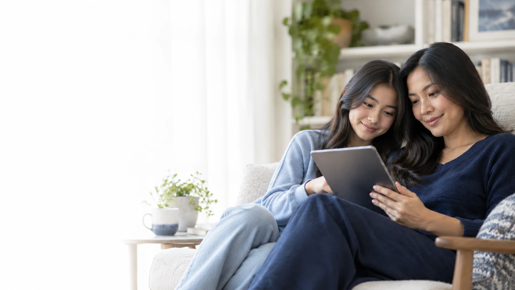 Ibu dan putri remajanya membaca ebook bersama melalui tablet di ruang baca yang terang